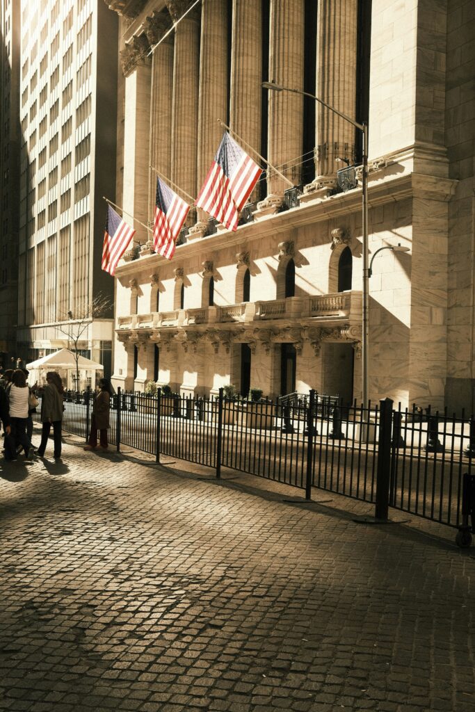 Historic building with American flags, cobblestone street, and pedestrians near a financial district, symbolizing investment and business.